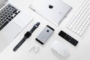 Flat lay of Apple devices including iPhone, iPad, MacBook, and Watch on a white surface, ideal for tech enthusiasts.
